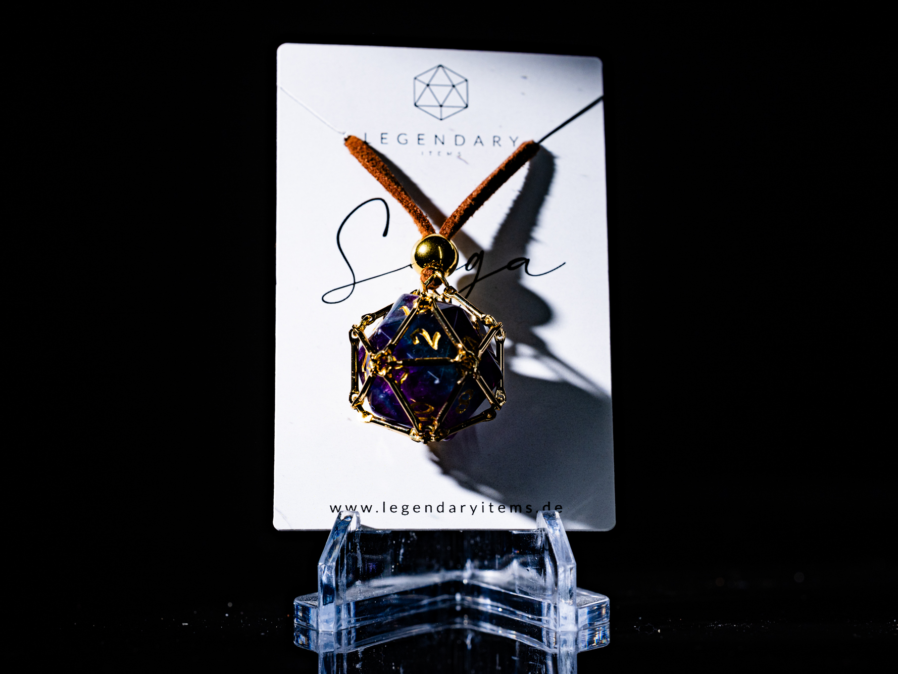 Angled macro shot of “Saga – Arcane Focus”: purple Amethyst D20 inside a golden dice cage on a brown PU leather necklace.